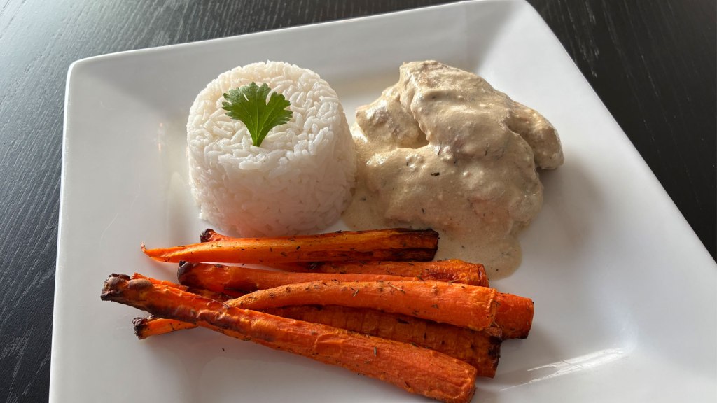 Ris, kylling i saus og stekte gulrøtter dandert på tallerken. Foto.